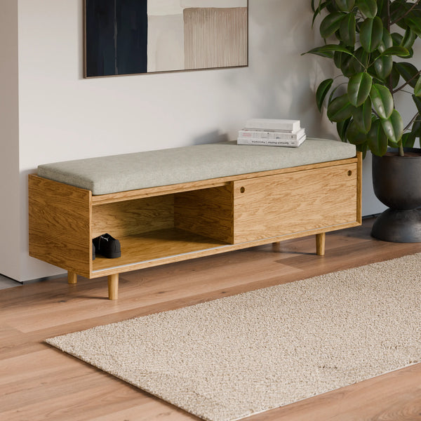 ספסל אחסון כניסה מעץ אלון בהיר עם מושב מרופד בגוון אפור-ירקרק ותא אחסון פתוח וסגור, משמש כפתרון פונקציונלי בקולקציית ספסלים מעוצבים לחדר כניסה או מסדרון.