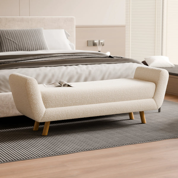 ספסל מרופד רחב בצבע שמנת, בעל משענות צד קמורות ורגלי עץ טבעי, המשמש כספסל נוי בקצה המיטה וכחלק מקולקציית ספסלים מעוצבים לחדר שינה.